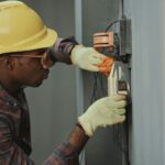 Elektriker mit Schutzhelm bei der Installation, dessen Aufträge ein CRM für Handwerker dokumentiert
