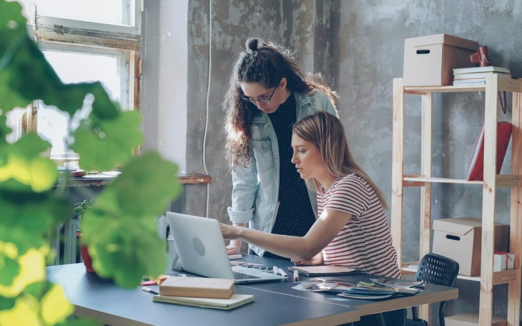 Zwei Kolleginnen besprechen am Laptop den Einsatz von KI-Tools für Unternehmen