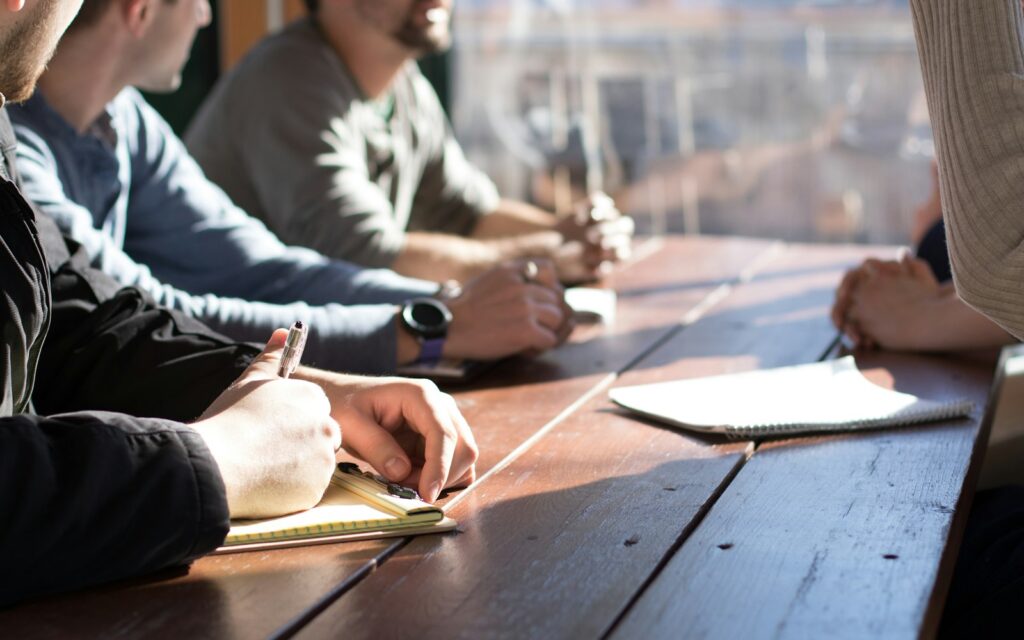 Menschen mit Stiften am Besprechungstisch: Abstimmung zwischen Marketing und Vertrieb