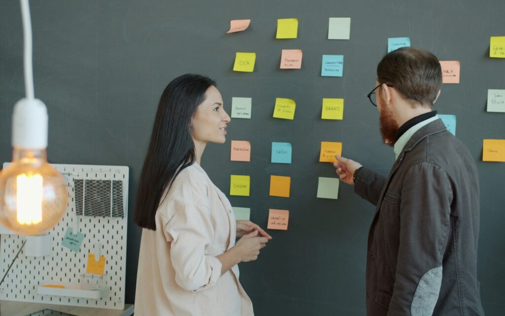 Zwei Kollegen sortieren Haftnotizen an der Wand zur Unique Selling Proposition