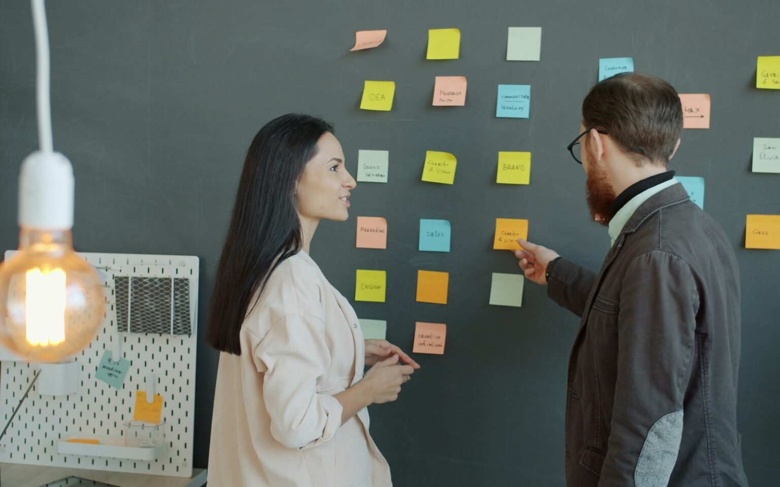 Zwei Kollegen sortieren Haftnotizen an der Wand zur Unique Selling Proposition